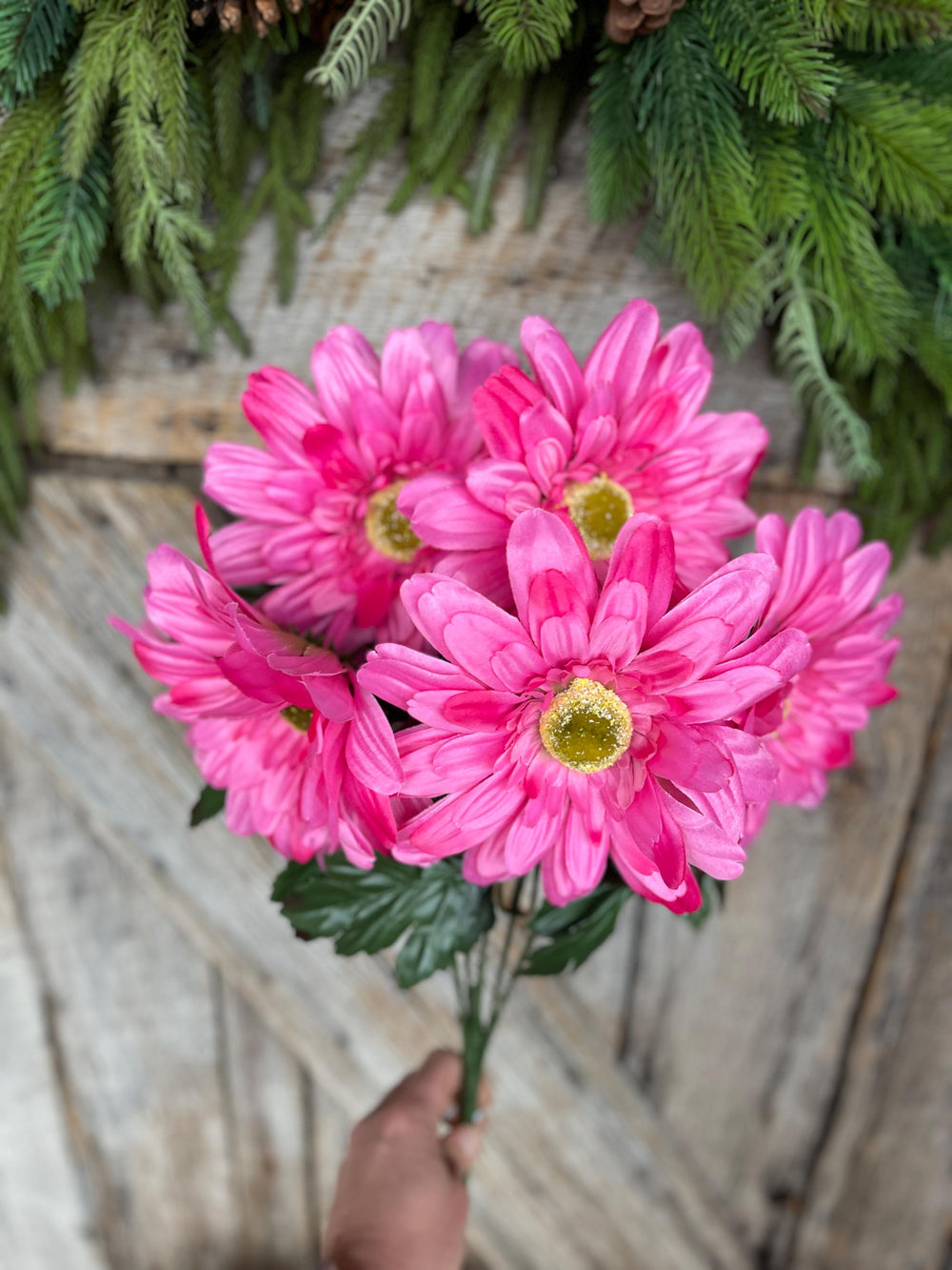 May include: A bouquet of pink gerbera daisies with yellow centers. The flowers are arranged in a bunch and have green leaves.