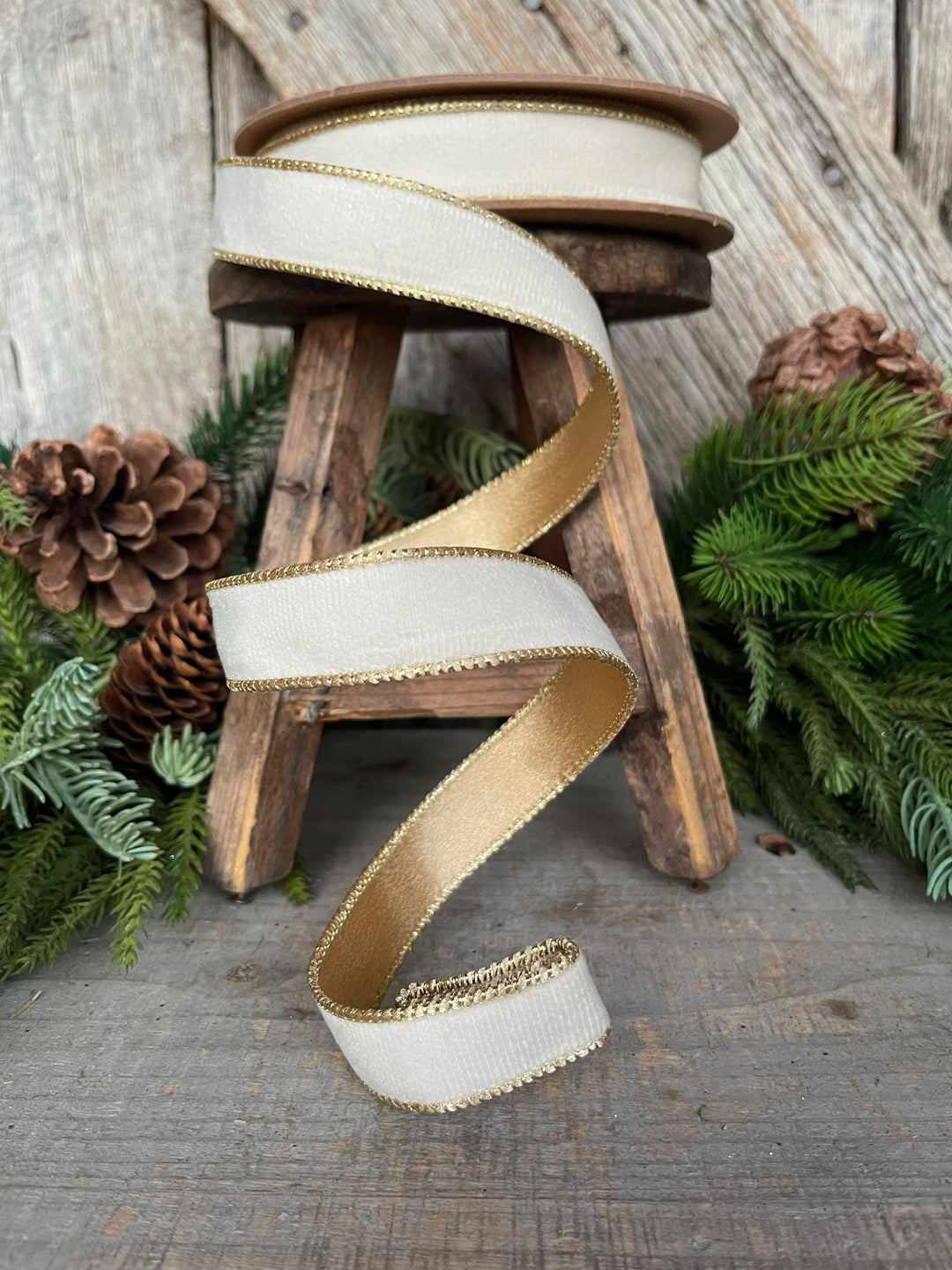 May include: White velvet ribbon with gold trim. The ribbon is wrapped around a wooden stool and is displayed against a rustic wooden background.