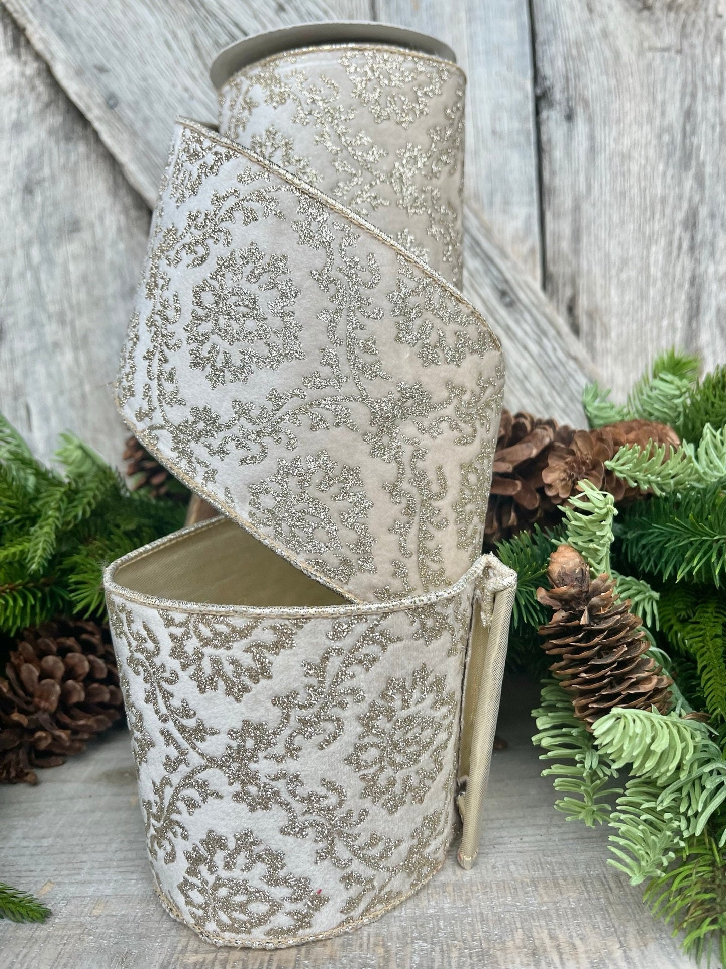 May include: Two rolls of white and gold glitter ribbon with a damask pattern. The ribbon is curled and stacked on top of each other.