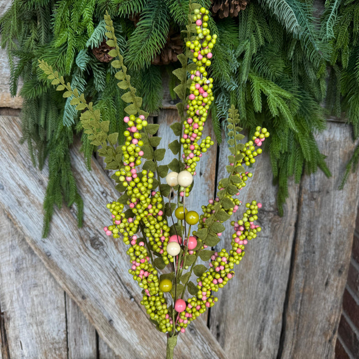 May include: A decorative floral stem featuring green leaves and clusters of small, round berries in shades of green, pink, and cream. The stem is set against a rustic wooden background and evergreen foliage.