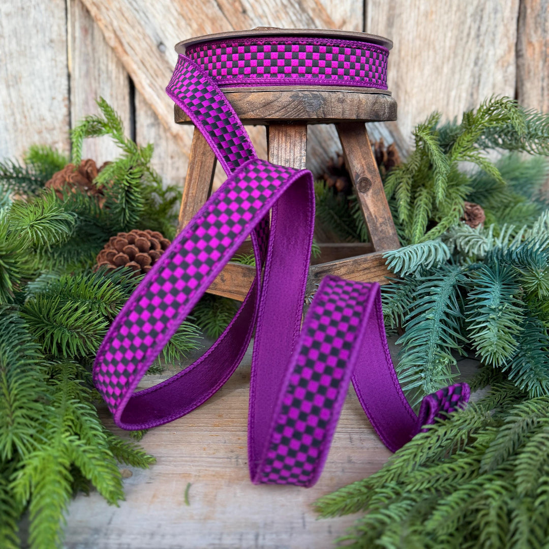 May include: A spool of ribbon featuring a vibrant purple and black checkered pattern on the front side and a solid purple color on the reverse. The ribbon is draped in loose folds, showcasing the contrasting colors and the woven texture.